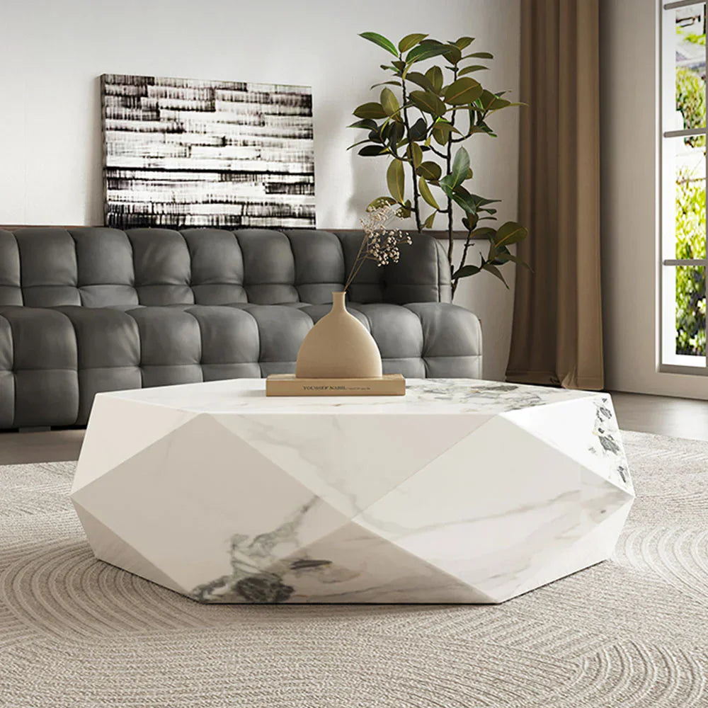 Geometric sintered stone coffee table with a faceted white surface, styled in a modern living room with a tufted sofa, soft rug, and natural daylight.