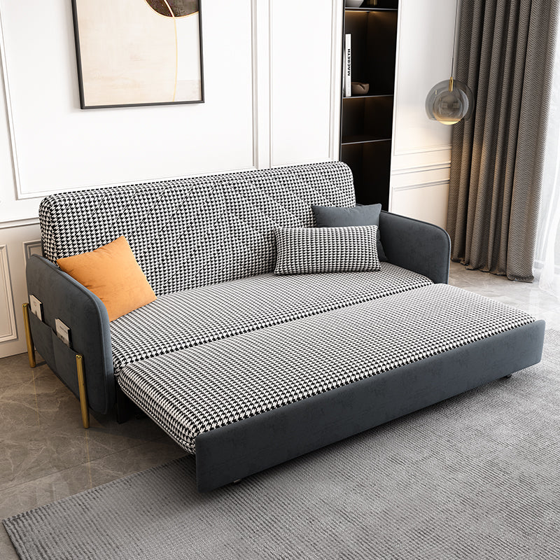 Gray and black checkered sofa bed in a room with a rug and wall art.